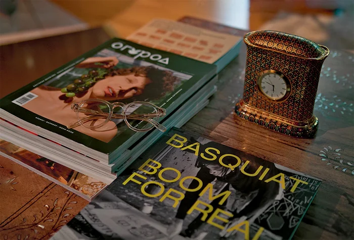 На столике — каталог выставки Ильи Кабакова, Basquiat: Boom for Real и весенний номер жур-нала «Огород». Часы —подарок родителей